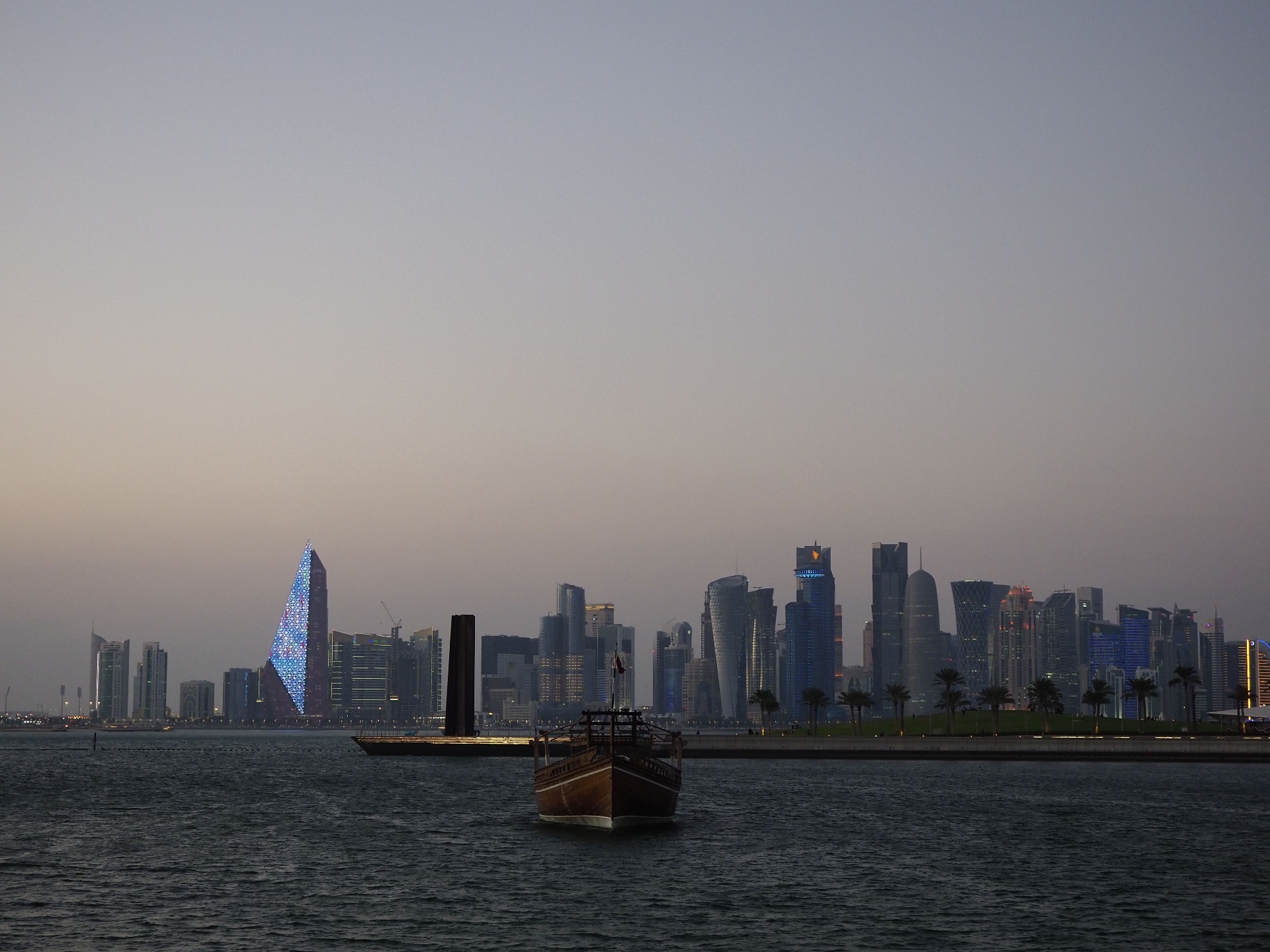 City skyline at dusk with a traditional dhow boat on the water